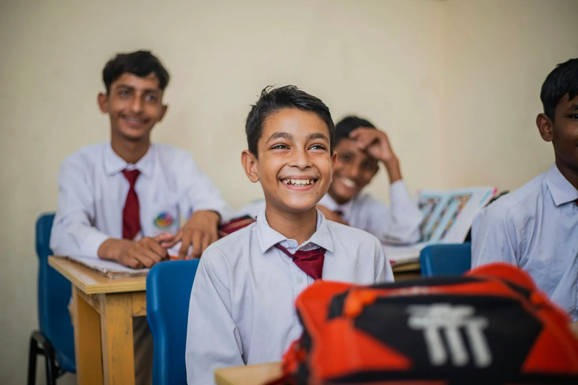 Schoolboys in white shirts and maroon ties laughing at their desks