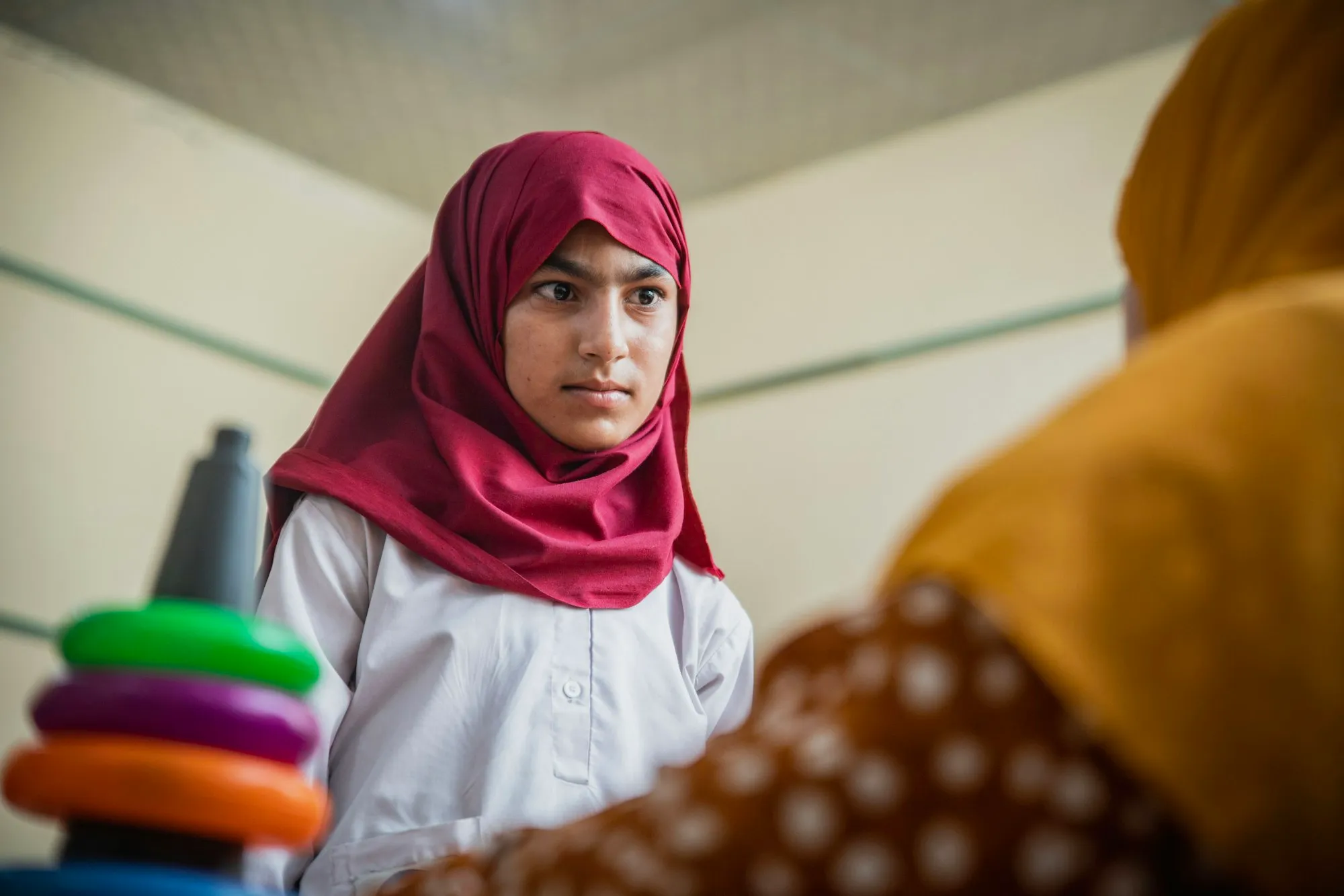 A student in a maroon hijab and white uniform in her classroom